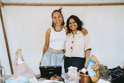 Portrait of smiling woman with arm around female partner standing in market stall