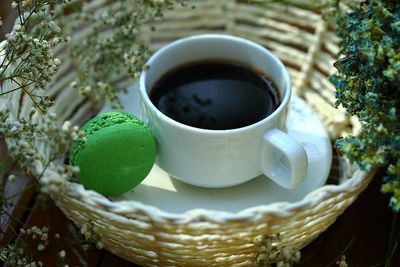 Black coffee with green macaroon on white basket.