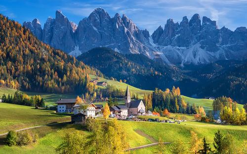 Scenic view of field by houses and mountains against sky