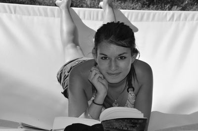 Portrait of young woman reading book while lying on hammock