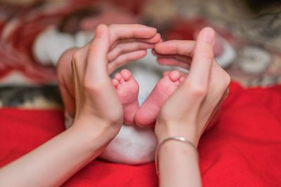 Cropped hands forming heart shape while holding baby feet on bed