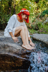 Full length of woman sitting on rock by flowing water