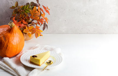 Halloween, thanksgiving concept with pumpkin pie piece, orange pumpkin, fall leaves on white table.