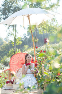 Young asian woman wearing a white dress poses with a rose in rose garden, chiang mai thailand