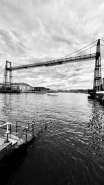 View of suspension bridge over river against cloudy sky