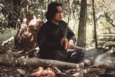 Young man sitting on tree trunk in forest