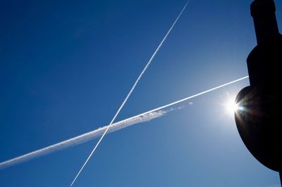 Low angle view of vapor trail against blue sky on sunny day