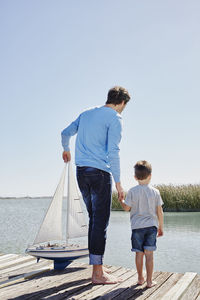Father with toy sailboat holding hand of son while standing on pier