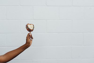 Cropped hand holding food against white wall