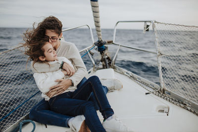 Mother kissing daughter while sitting on sailboat