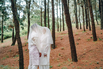 Bride and bridegroom standing amidst trees in forest