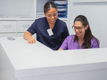Female nurses in scrubs smiling while working behind counter on reception of modern clinic