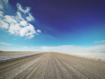 Low angle shot of gravel road on a blue sky winter day in rural, unfenced farmland.