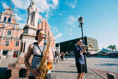 People playing on street in city against sky