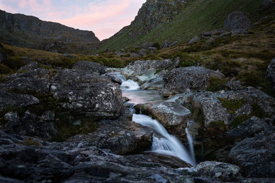 Scenic view of waterfall by sea against mountain