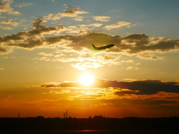 Silhouette of birds flying against cloudy sky during sunset