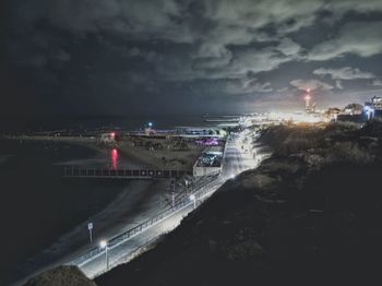 Illuminated city by sea against sky at night