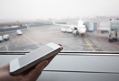 Cropped image of hand holding smart phone against glass window