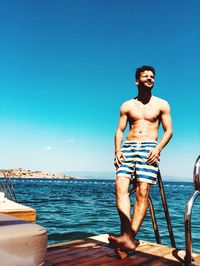 Full length of shirtless man standing on boat in sea against sky