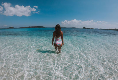 Rear view of woman standing on beach against sky