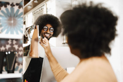 Smiling male hairdresser selling beauty product to female customer in salon