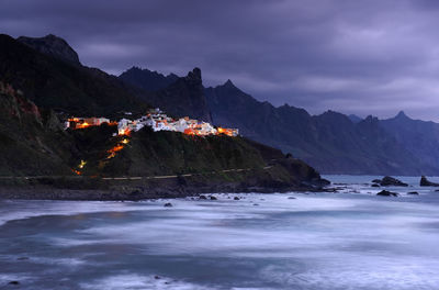 Mountains by sea against cloudy sky during sunset