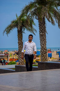 Full length portrait of young man standing against palm trees