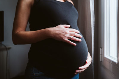 Midsection of pregnant woman standing at home