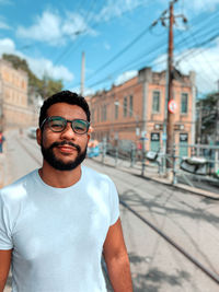 Portrait of young man standing in city against sky
