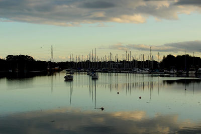 Sailboats moored at harbor against sky during sunset