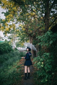 Full length of woman holding umbrella while standing on footpath in forest