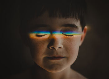 Close-up of cute boy with spectrum on closed eyes in darkroom at home