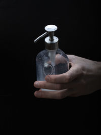 Close-up of hand holding glass bottle against black background