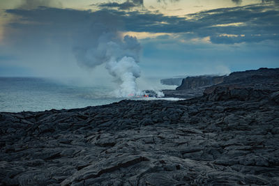 Smoke emitting from volcanic crater by sea against sky