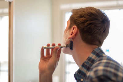 Close-up of young man shaving at home