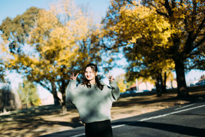 Smiling young woman showing peace signs while standing on road