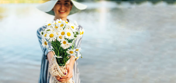 Young woman holding flower bouquet against lake