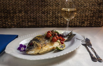 Close-up of grilled dorado in plate served with wineglass on table