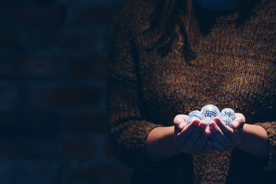 Close-up of woman holding shiny balls in darkroom