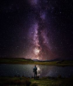 Rear view of man standing by lake against star field