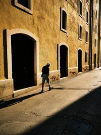 Rear view of man walking on street by building