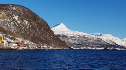 Scenic view of sea and snowcapped mountains against clear blue sky