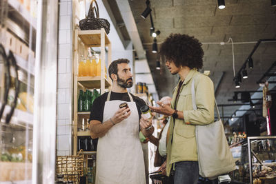 Salesman and young male customer discussing over jars at grocery convenience store