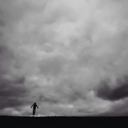 Silhouette person levitating on field against cloudy sky