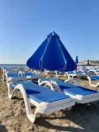 Deck chairs and parasols on beach against clear blue sky