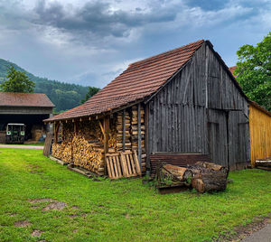 Old barn on field by building against sky