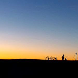 Silhouette people riding bicycle on field against clear sky during sunset
