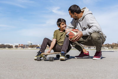 Father and son with longboard and basketball outdoors