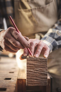 Midsection of carpenter measuring wood in workshop