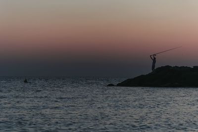 Silhouette person fishing in sea against sky during sunset